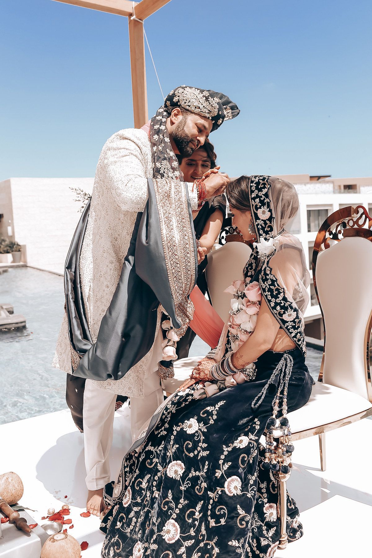 A tender moment between a couple in elegant Indian wedding outfits against a bright white backdrop.