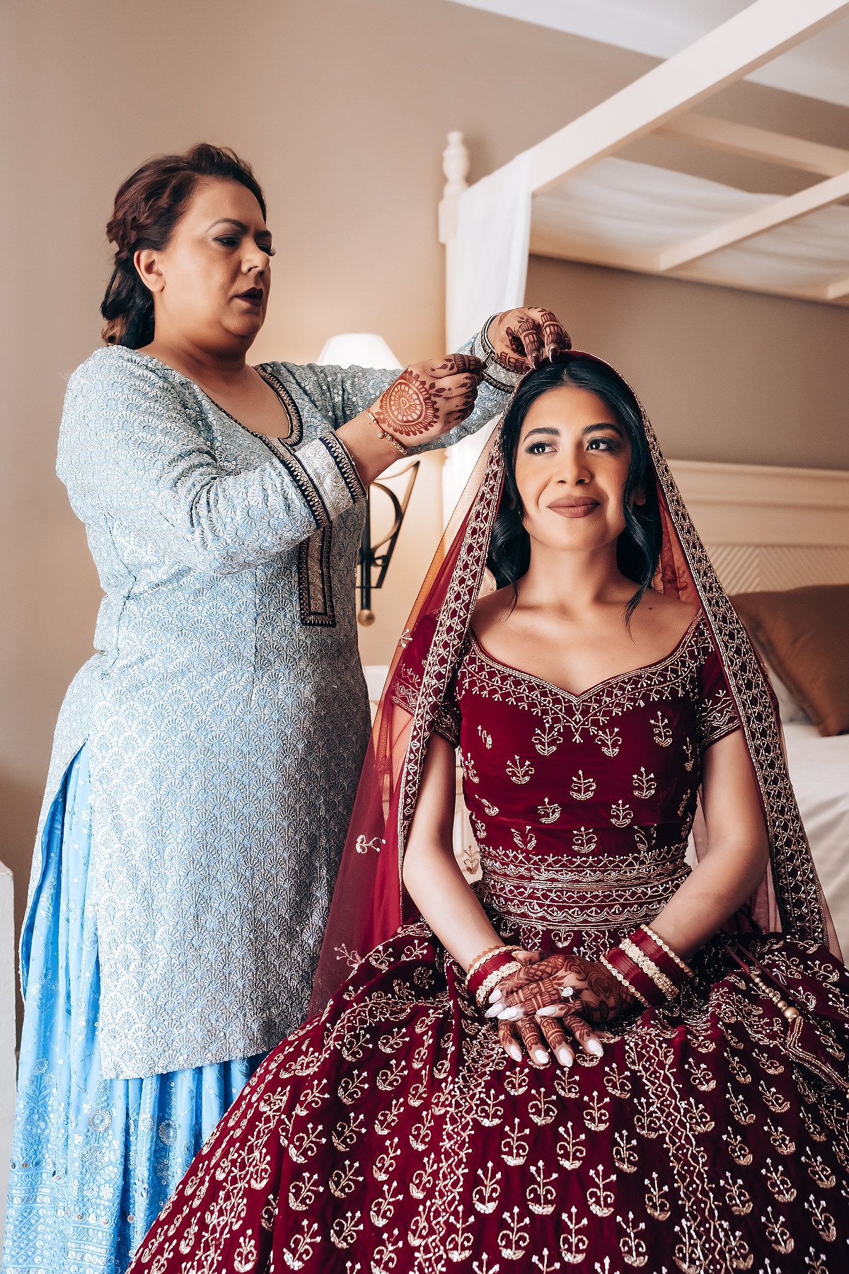 Traditional Indian bridal preparation scene with burgundy lehenga and styling assistance.