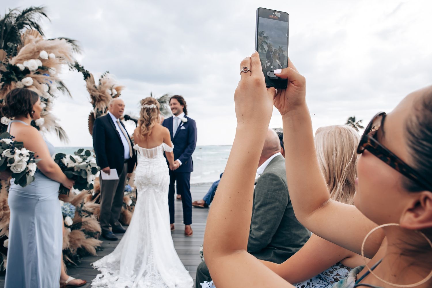 Wedding guests holding up phones to capture photos during an outdoor ceremony.