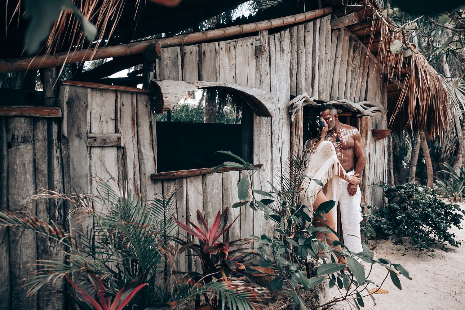 A romantic photoshoot outside a rustic beach hut surrounded by tropical plants.