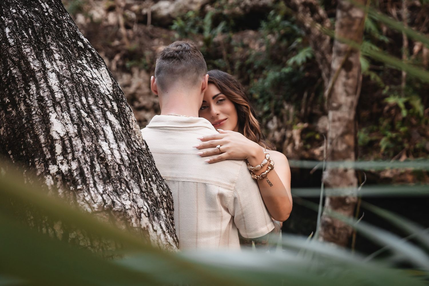 Intimate couple photos captured against rustic tree trunk in tropical garden setting.