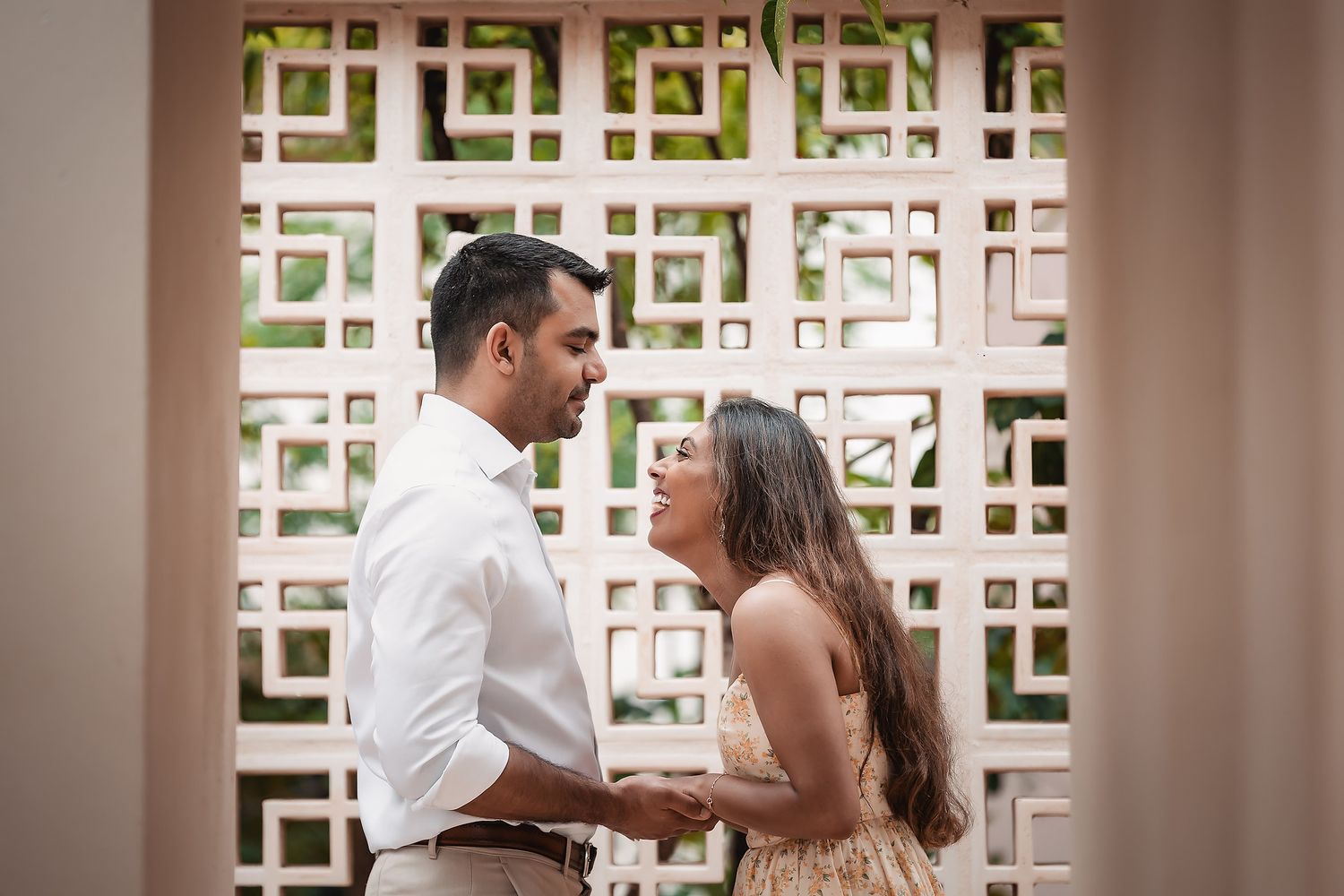 Couple poses together in front of decorative lattice wall during photoshoot.