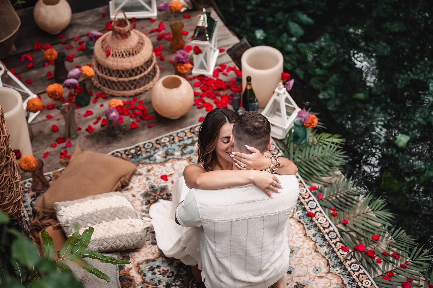 Couple sharing intimate moment on decorated platform with lanterns and rose petals.