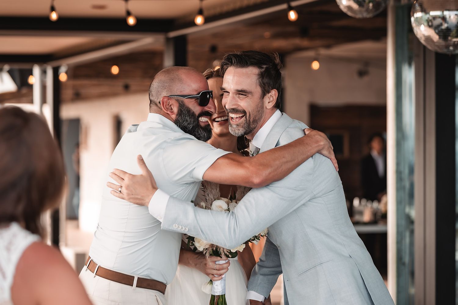 Wedding reception party with guests embracing and dancing under indoor lighting.