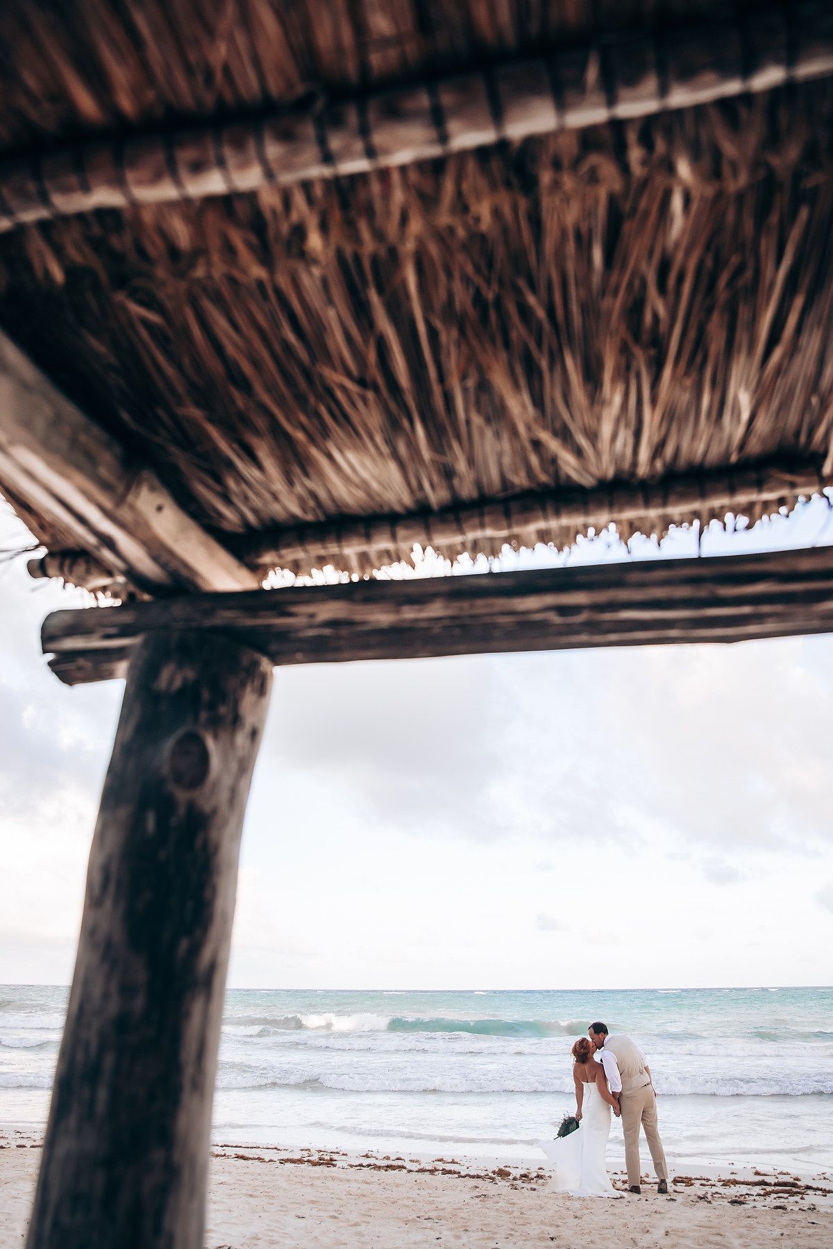Thatched beach pavilion overlooking the ocean with figures in the distance.