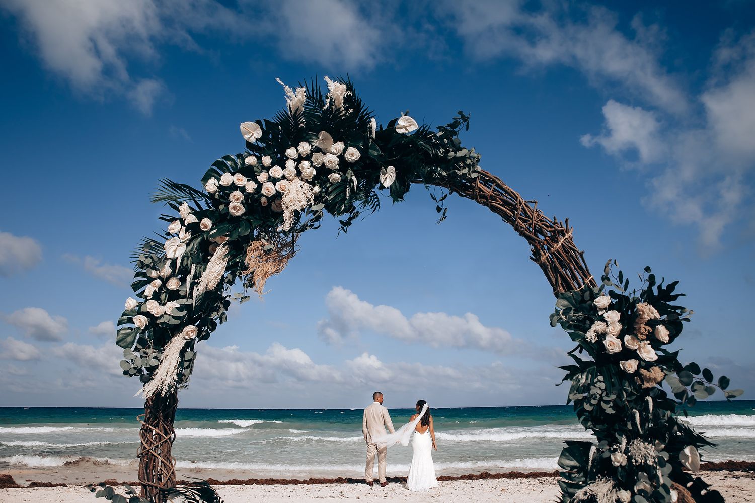 Elegant beach wedding arch decorated with white flowers against crystal blue waters.