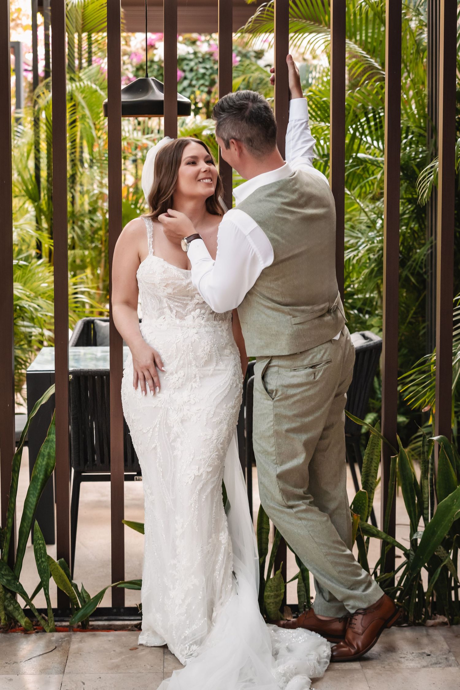 Couple shares playful moments between wooden fence posts surrounded by tropical plants.