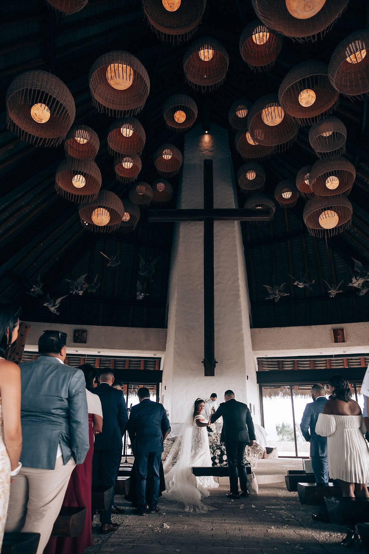 Large circular pendant lights hang from dark ceiling above cross in modern church interior.