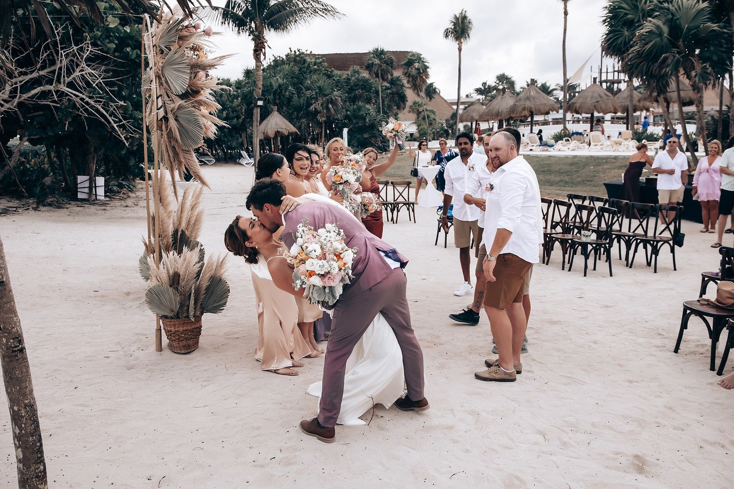 Wedding attendees gathered on a sandy beach with palm trees during an outdoor celebration.