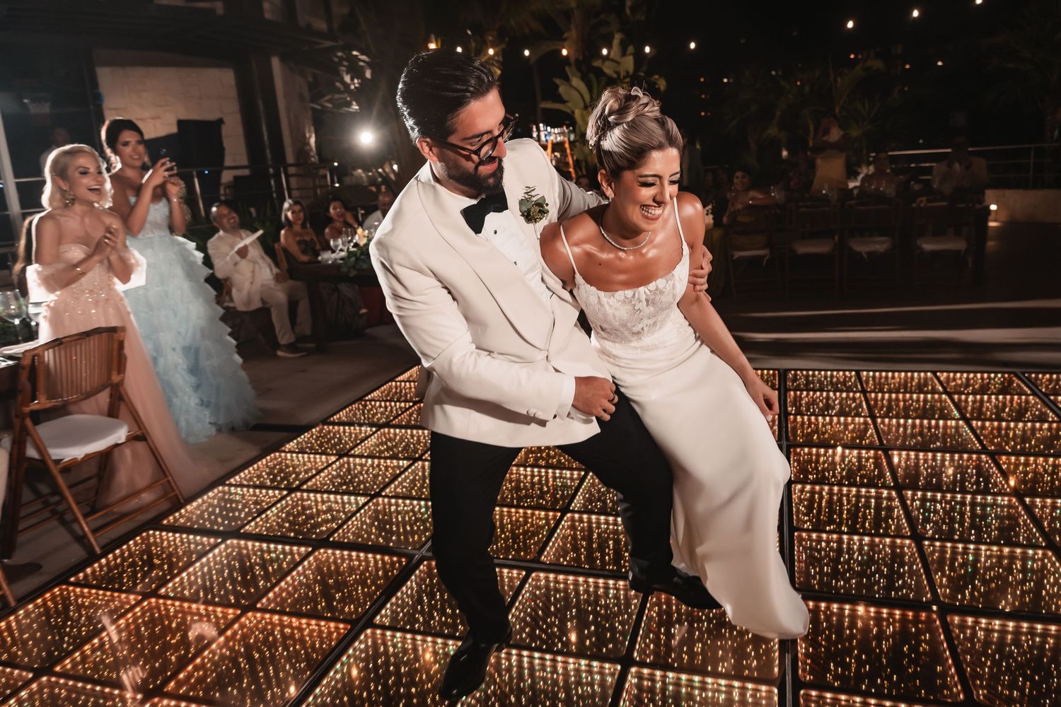 Romantic dance moves captured during a nighttime wedding reception on a lit-up dance floor.