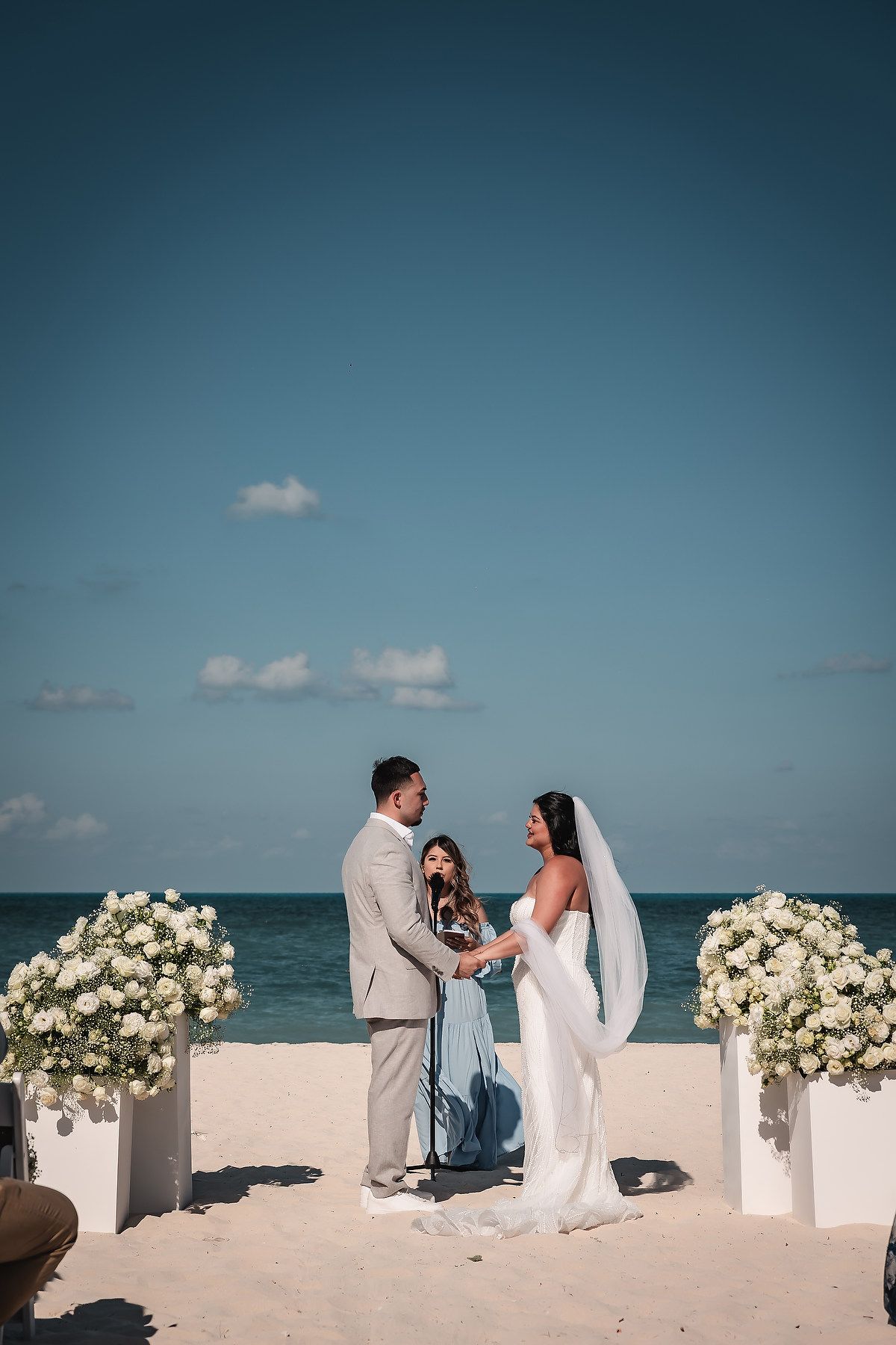 Romantic beach wedding ceremony with white floral arrangements and ocean backdrop.