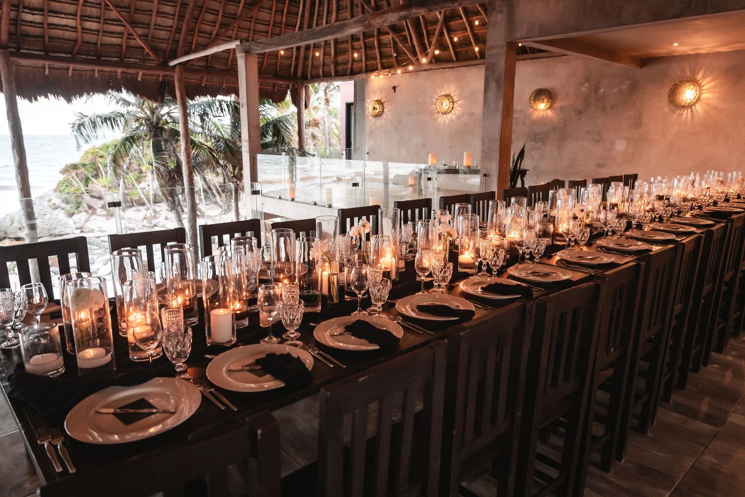 Elegant wedding reception setup under thatched roof with long tables and ambient lighting.