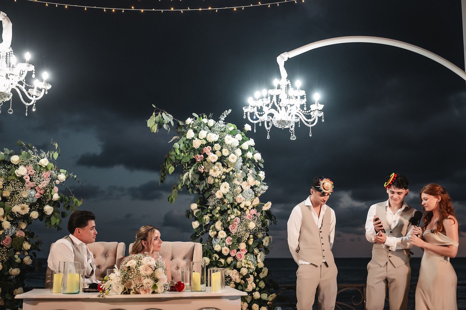 Evening reception under crystal chandeliers and floral arches with twinkling lights.