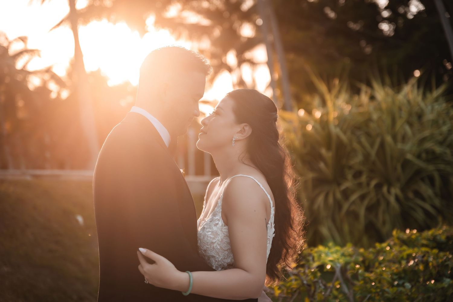 Romantic sunset wedding portrait with couple embracing among palm trees and golden light.