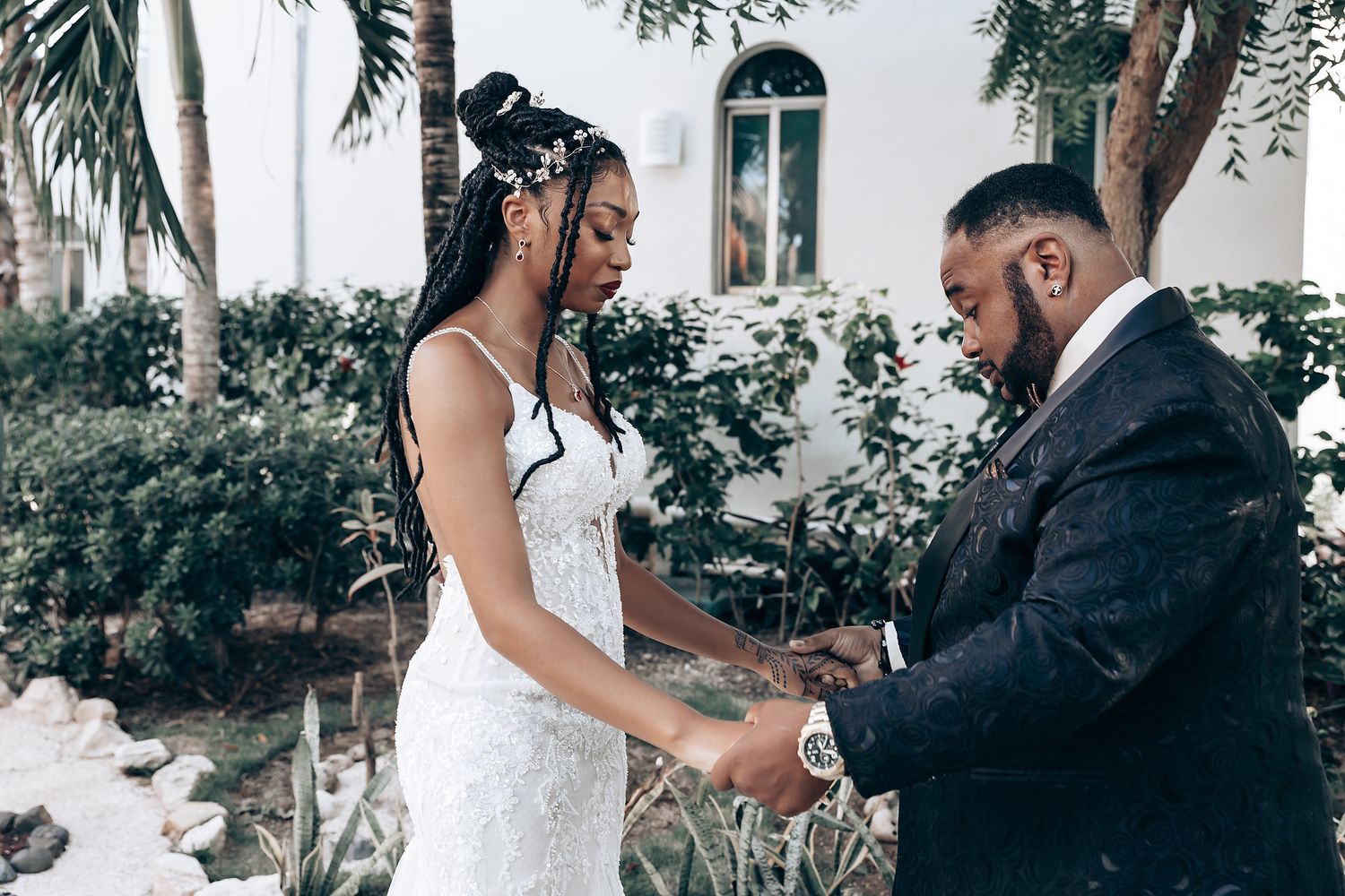 A couple shares an intimate moment during their outdoor wedding ceremony under palm trees.