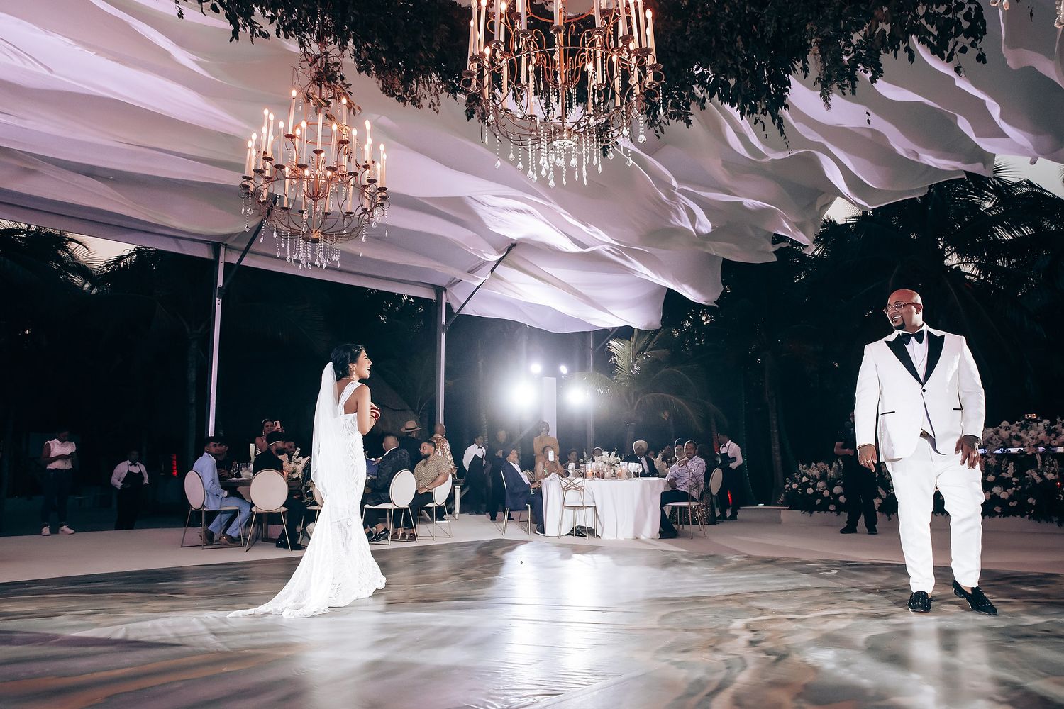 Elegant ballroom wedding reception with dramatic lighting and crystal chandeliers overhead.