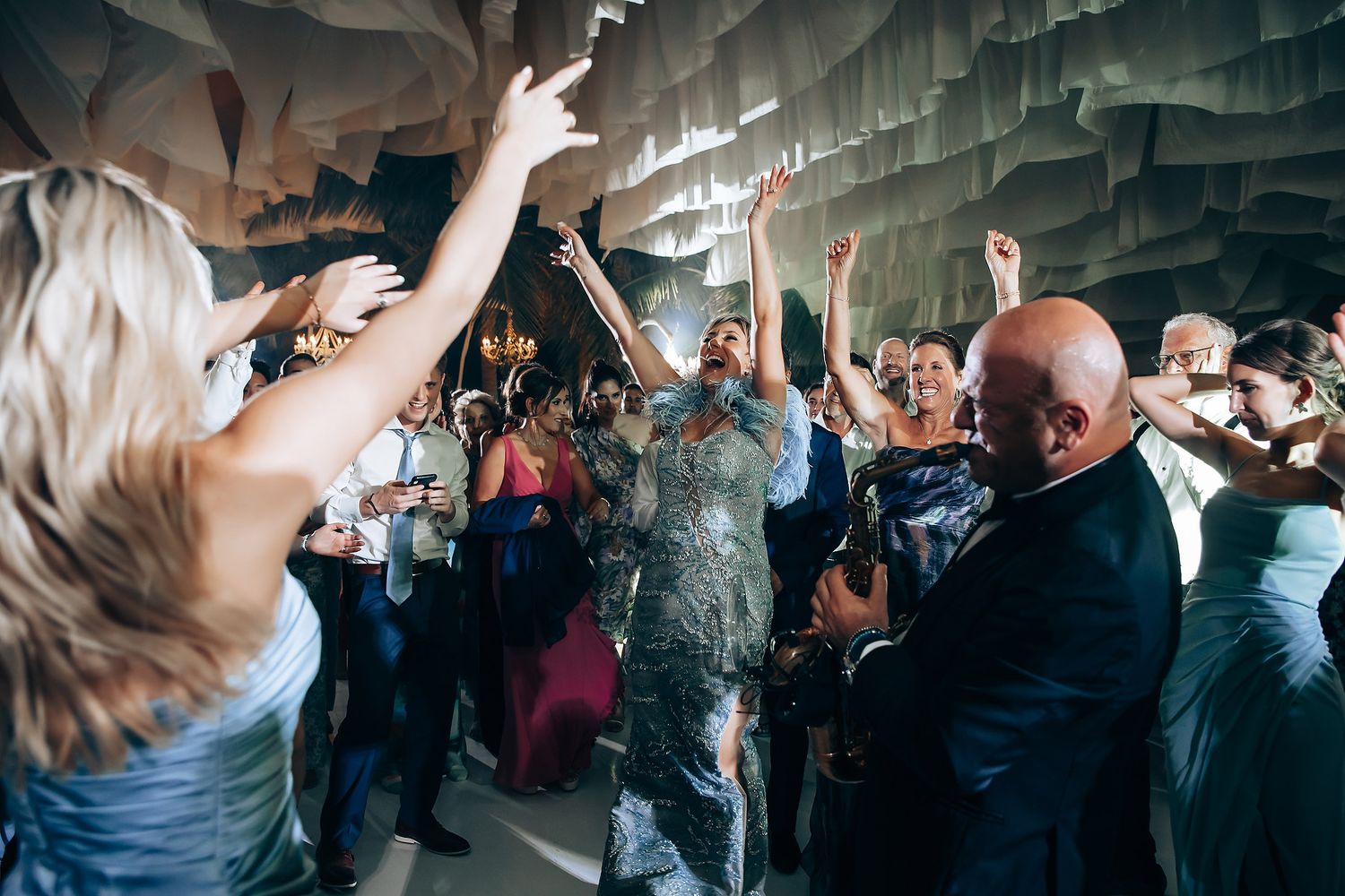 Wedding reception dance party with guests celebrating under draped fabric ceiling.