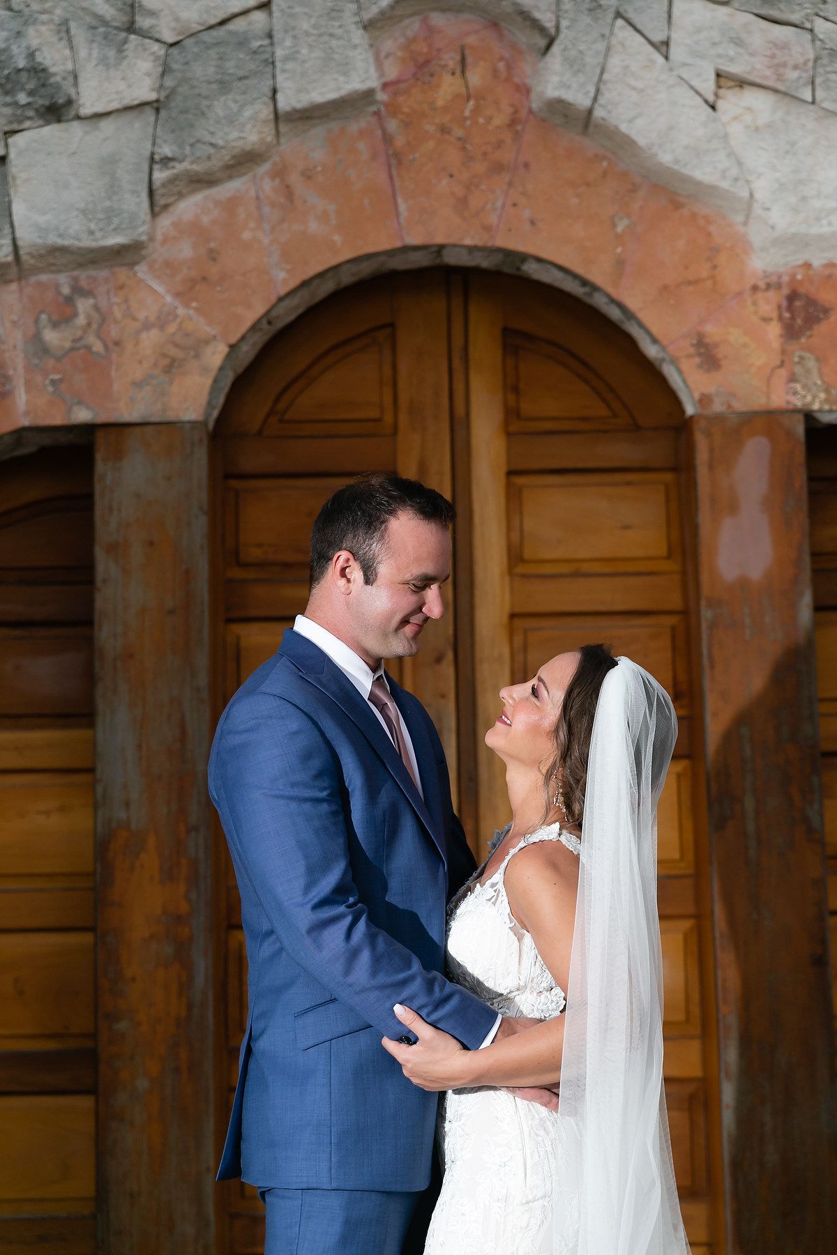 Wedding couple shares intimate moments against rustic wooden doors and weathered stone walls.
