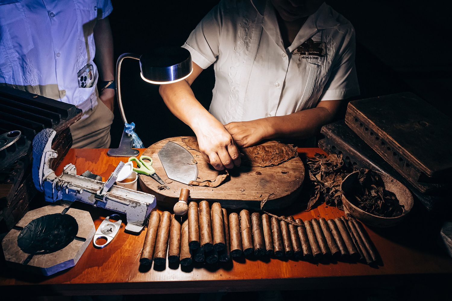 Multiple hands work at a wooden table with tools and equipment for leather crafting and repair.
