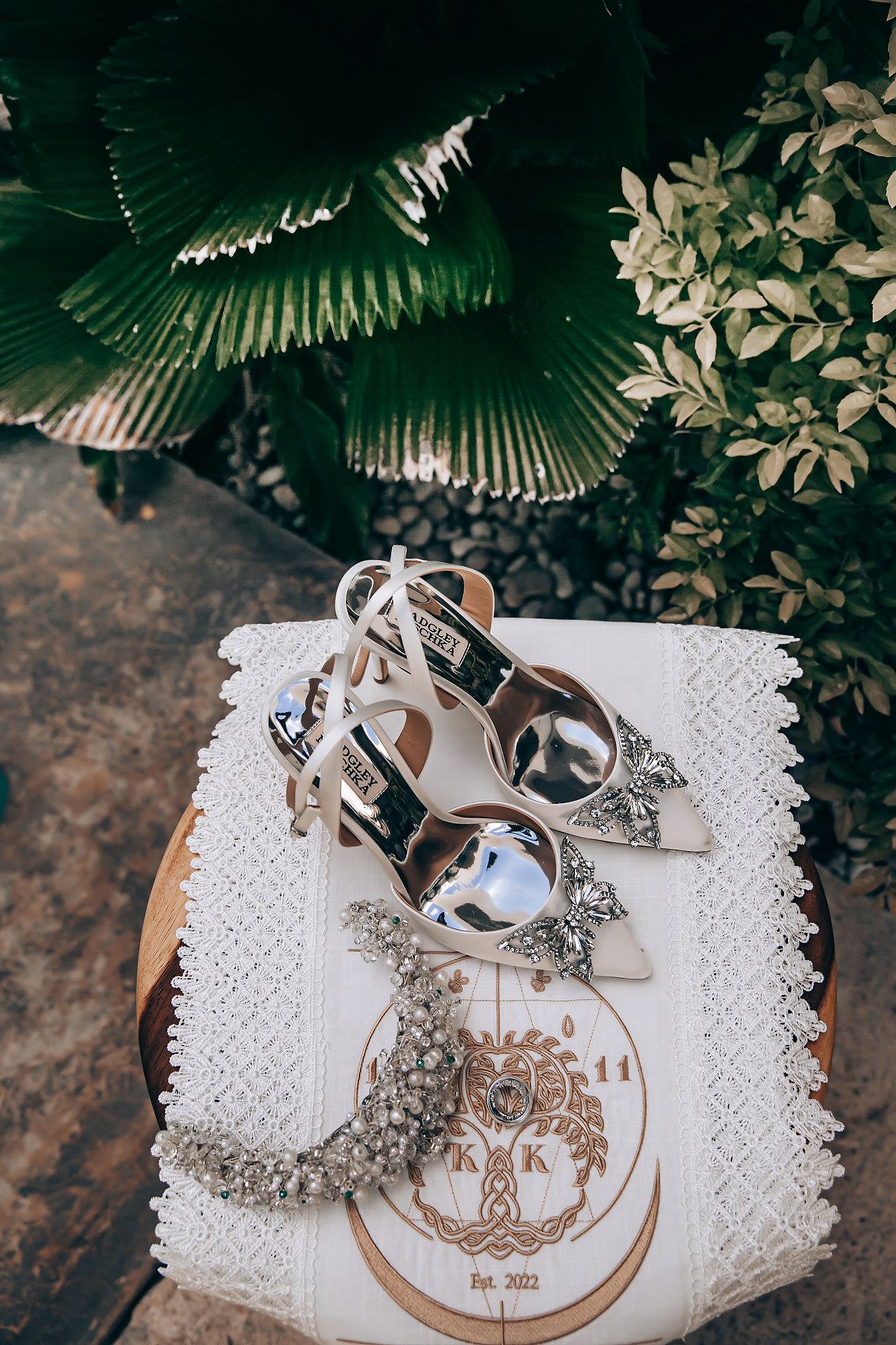 Wedding rings displayed on a white lace surface with decorative embroidered monogram design in natural lighting.