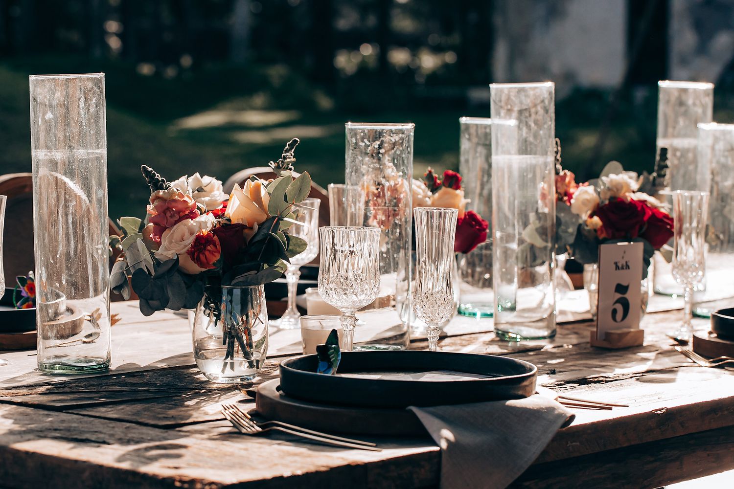 An elegant table setting with crystal glasses, black plates, and floral centerpieces in a modern dining space.
