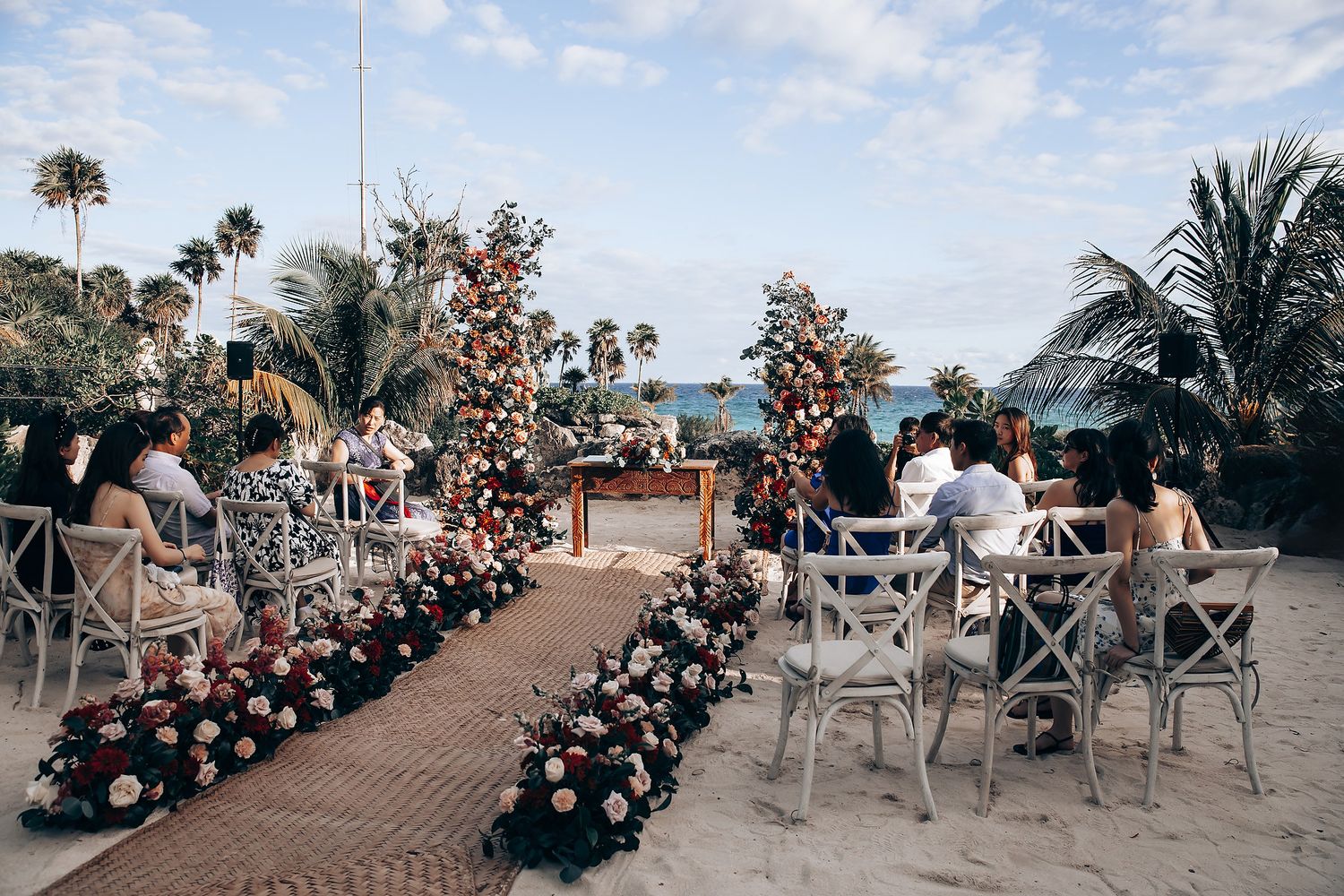 Outdoor beach wedding ceremony setup with white chairs and tropical palm trees under blue skies.