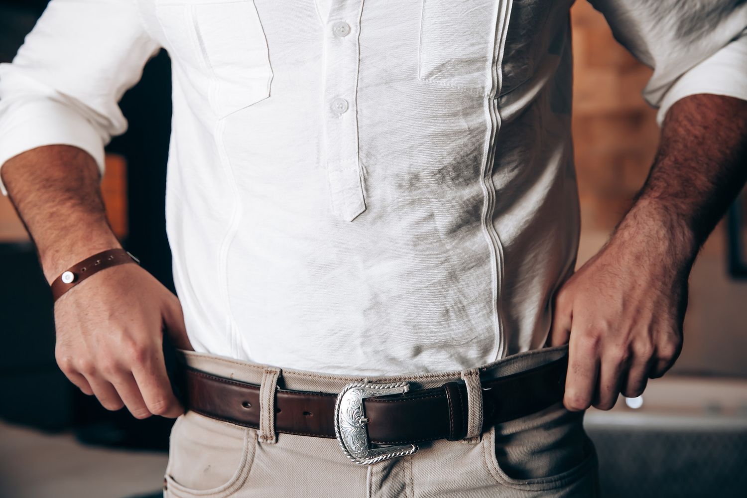Close-up of person wearing white shirt and brown leather belt with silver buckle.