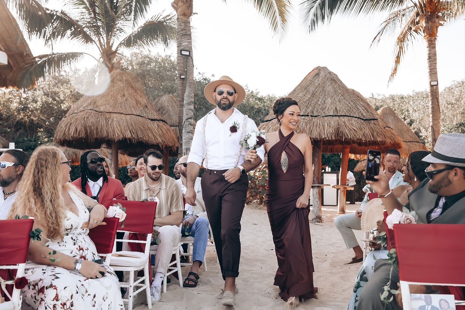 Beach wedding ceremony setup with palm trees and thatched roof huts in the background.