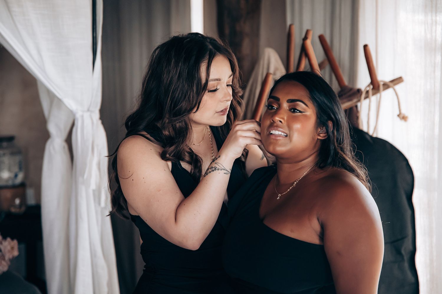 Emotional wedding preparation moments between two women in a sunlit room with white curtains.