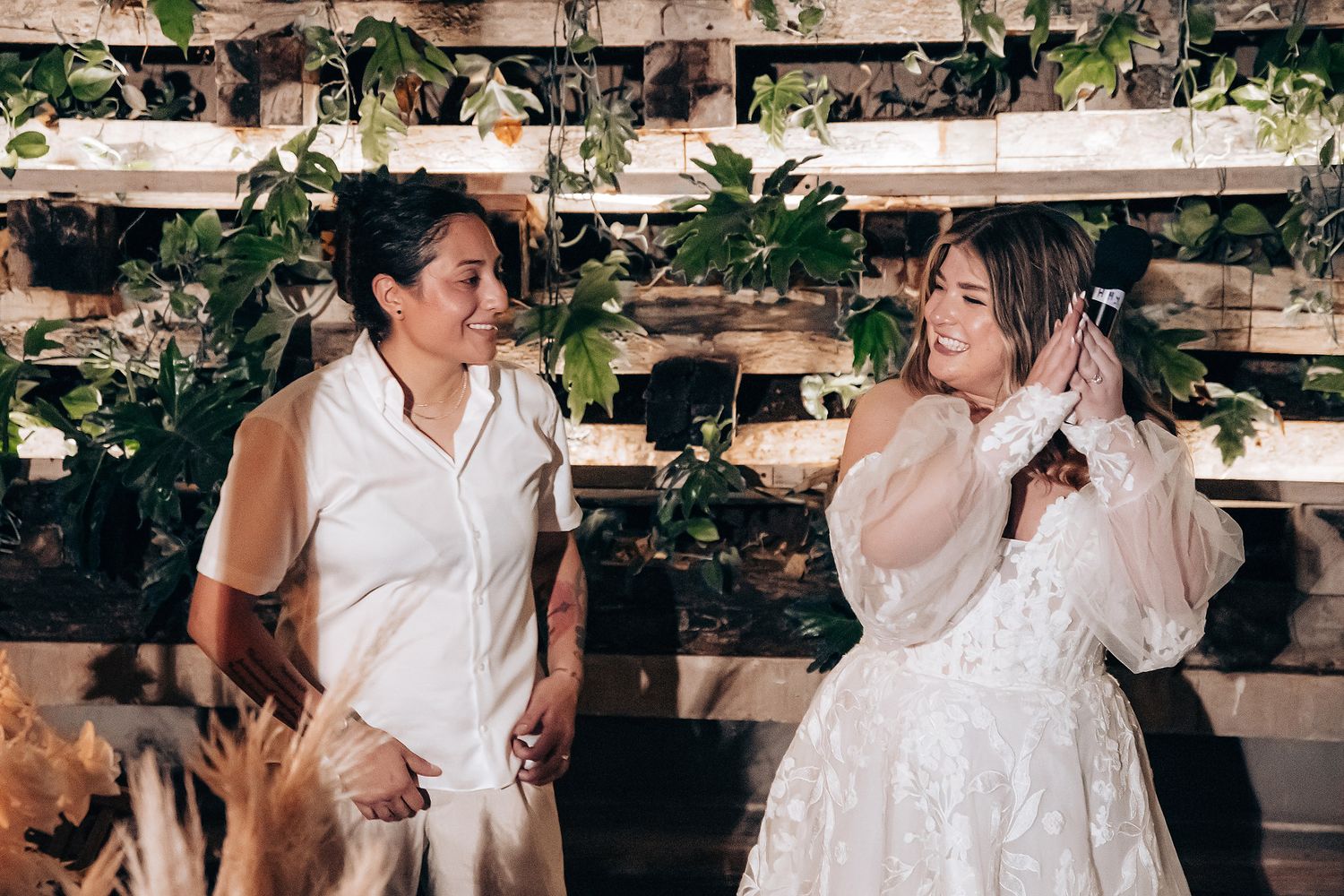 People sharing joyful moments at an outdoor wedding reception with greenery decorations.