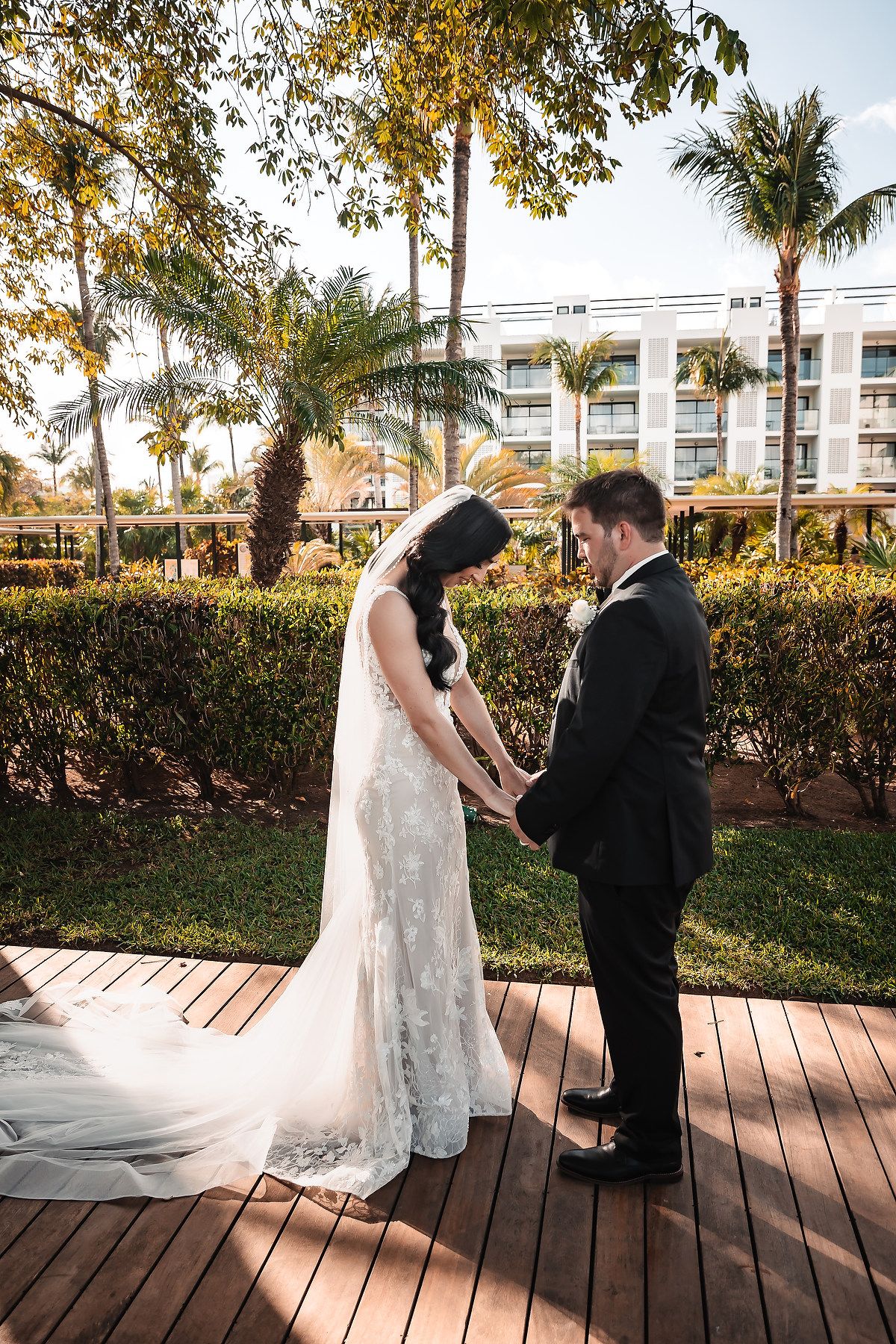 Emotional first look wedding photos captured on a wooden deck with palm trees in the background.