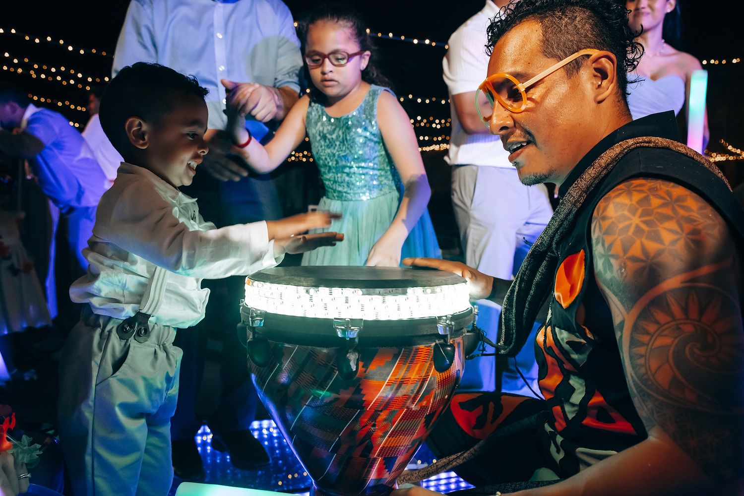 Wedding reception party scene with guests dancing under blue lighting and string lights.