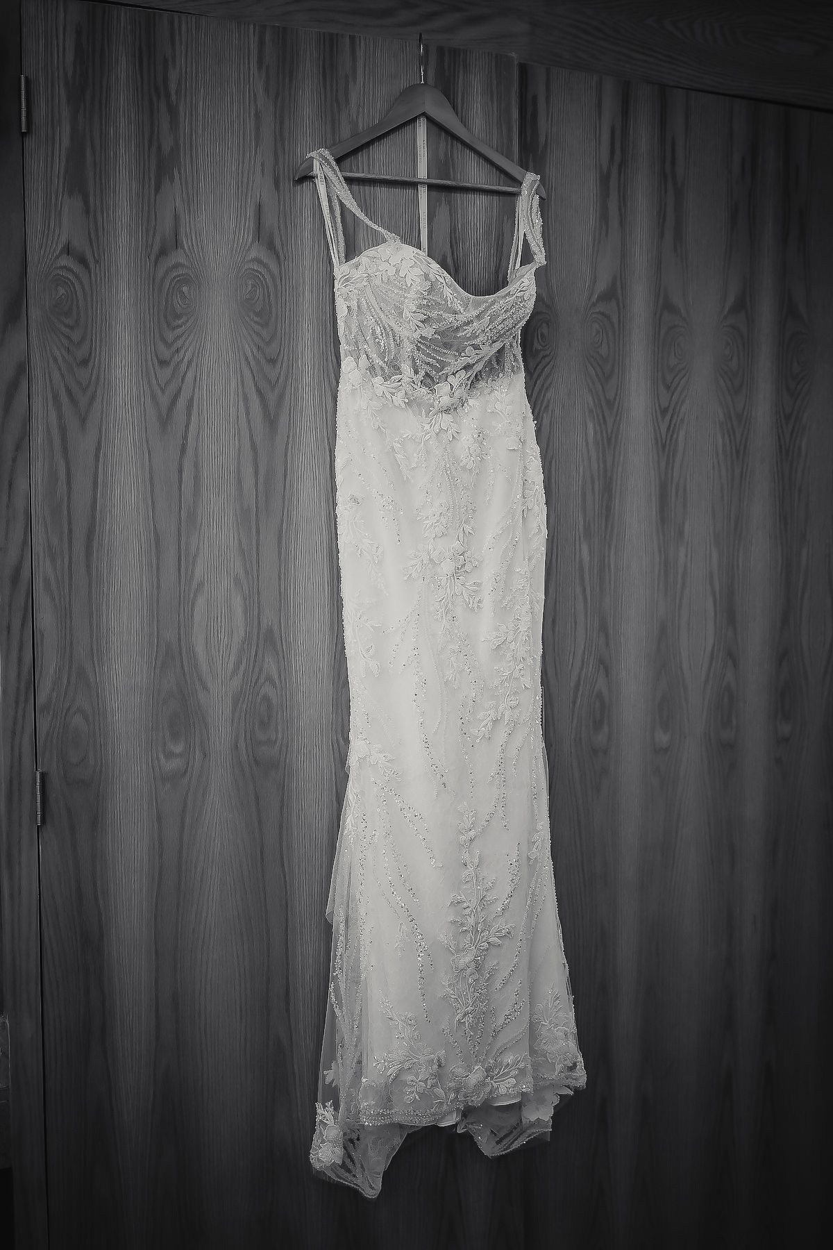 Elegant white lace mermaid wedding dress hanging on a wooden door in black and white photo.