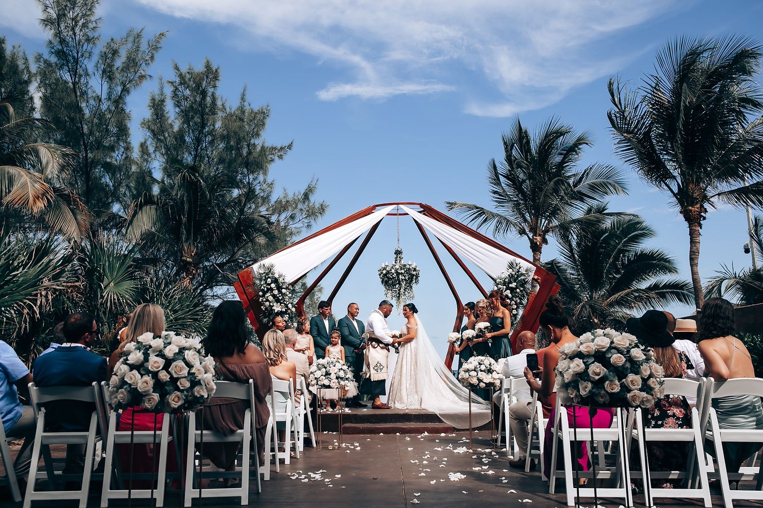 Panoramic view of a beach wedding ceremony with guests seated under blue skies.