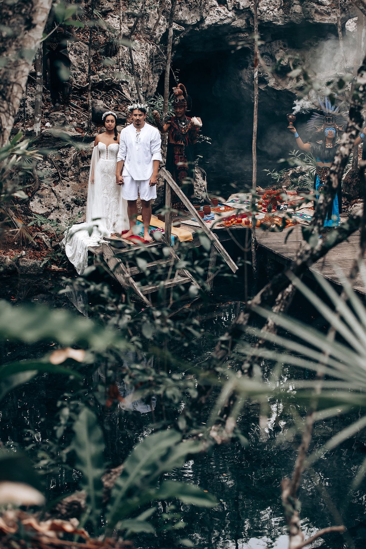 Wedding photo session in a tropical garden setting with dark stone walls and palm fronds in the foreground.