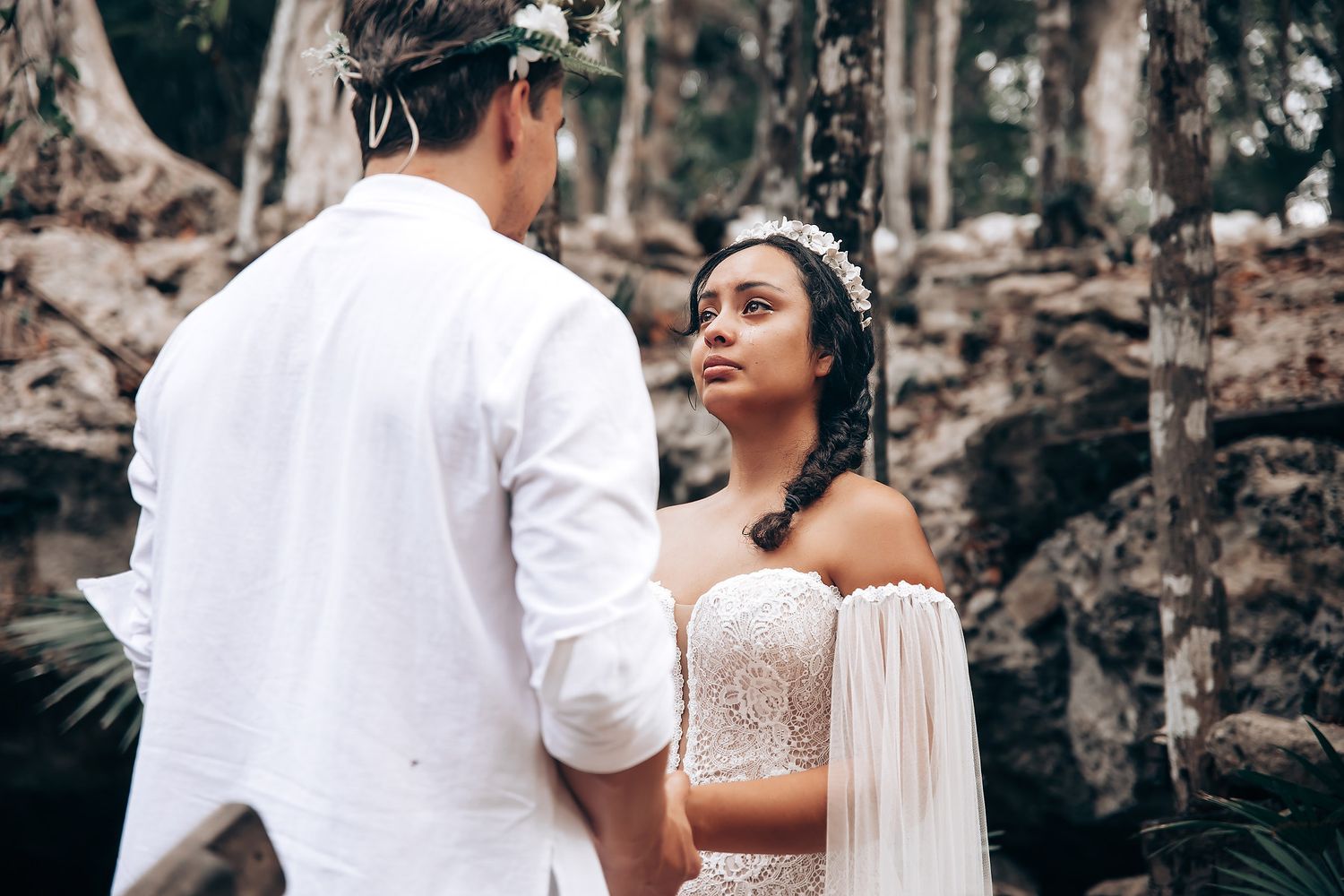 A couple in wedding attire shares an intimate moment in front of a stone wall during their outdoor ceremony.