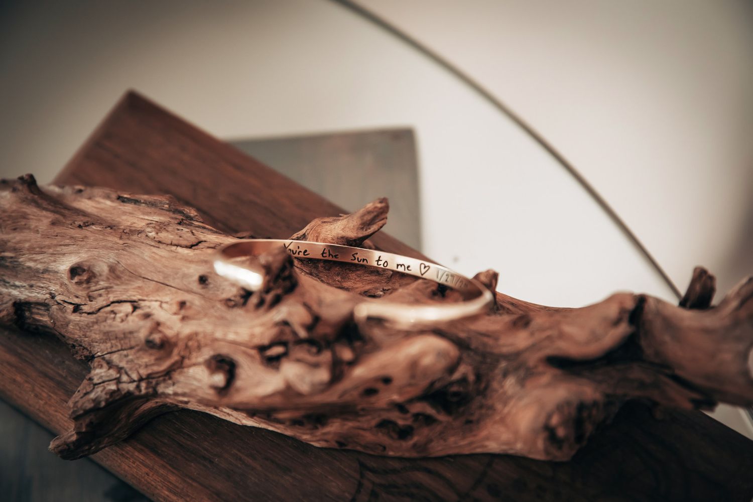Rose gold engraved cuff bracelet resting on rustic driftwood piece on wooden surface.