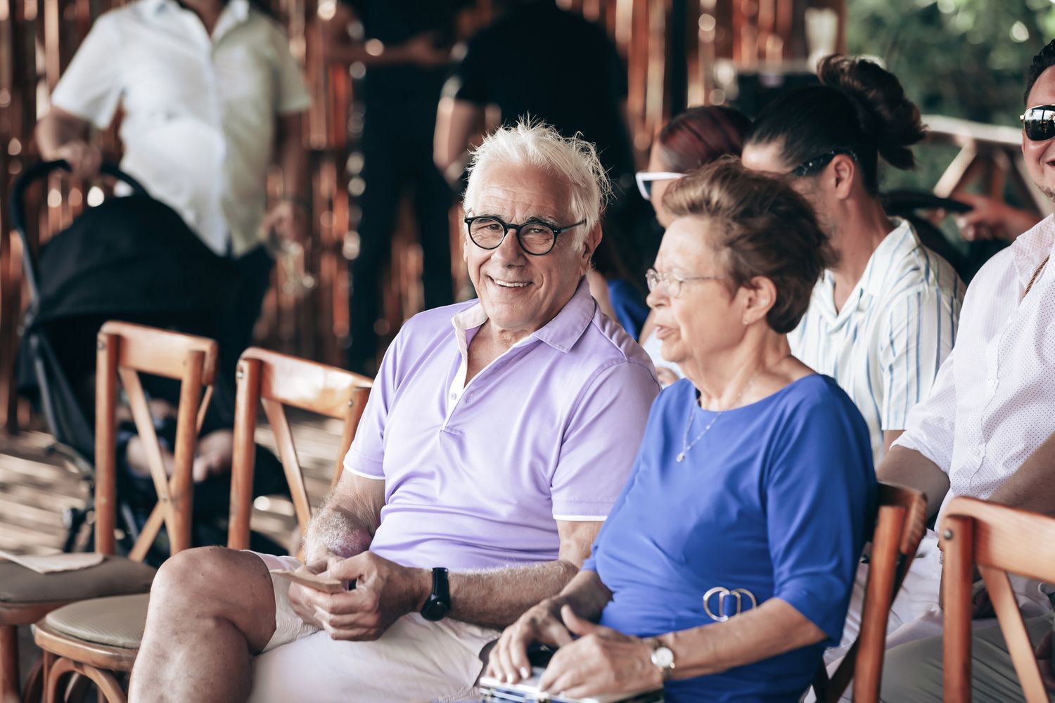 Happy elderly couple smiling and seated together at an outdoor wedding reception celebration.