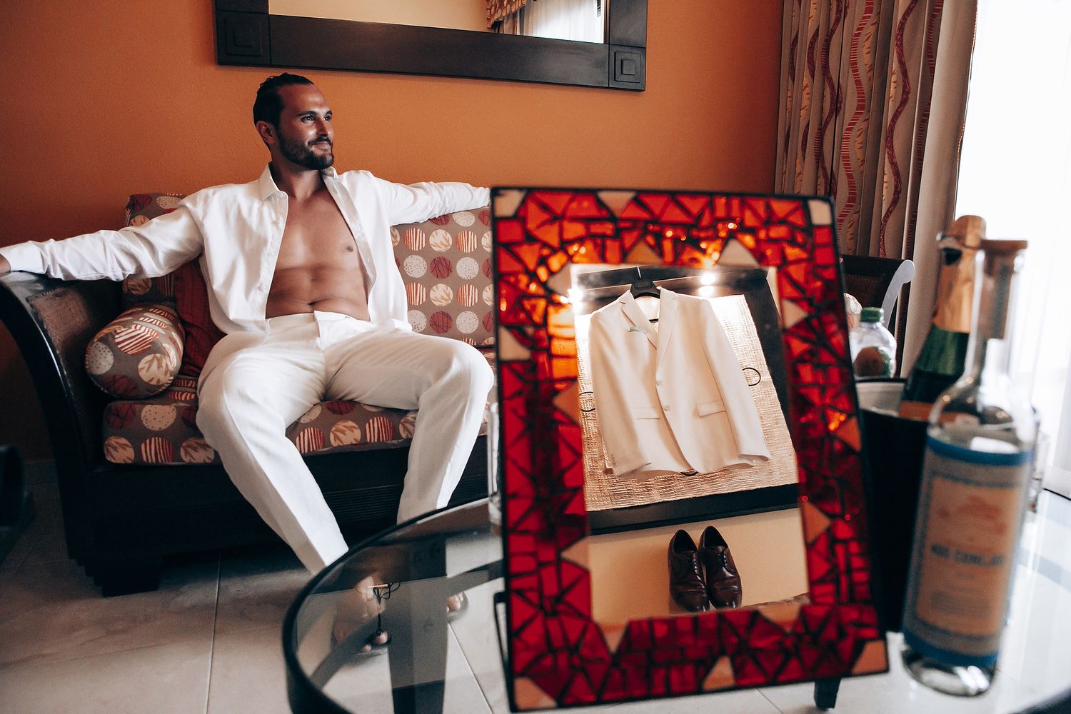 A person in formal attire poses on a red couch in a modern interior setting.