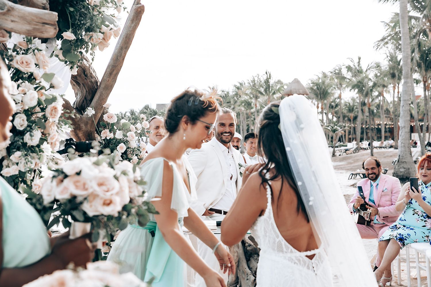 Wedding guests celebrating on a sunny beach with palm trees in the background.