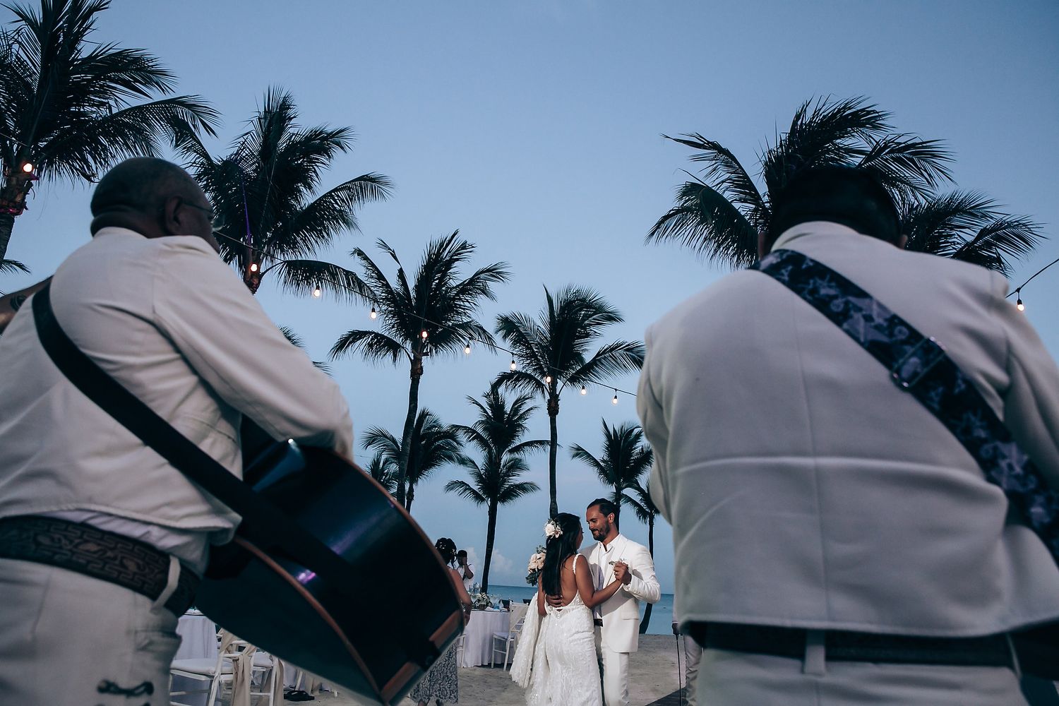 Tropical beach wedding ceremony with white chairs and palm trees swaying in the ocean breeze.