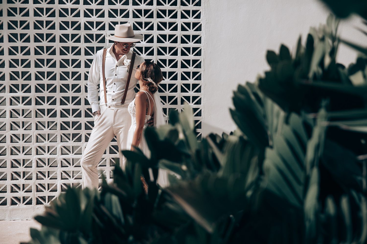 Modern architectural wall with geometric patterns and tropical plants creating shadows.