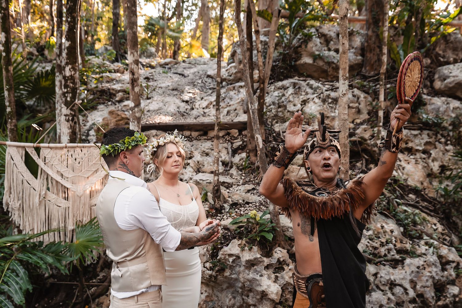 Couple exchanges vows in jungle cenote wedding with Mayan shaman officiant in traditional feathered costume.