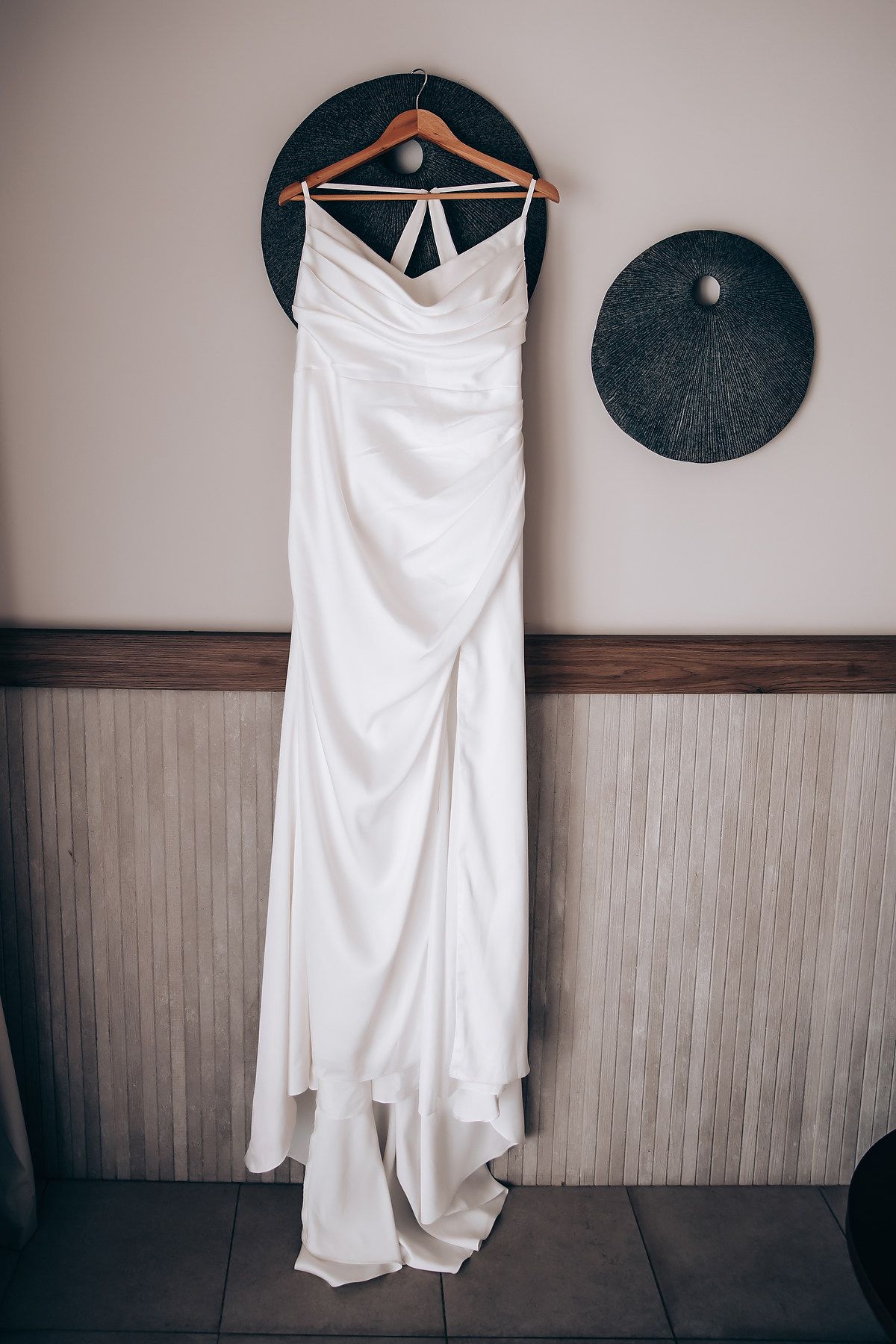White wedding dress hanging on wall next to dark circular decor piece in minimalist setting.