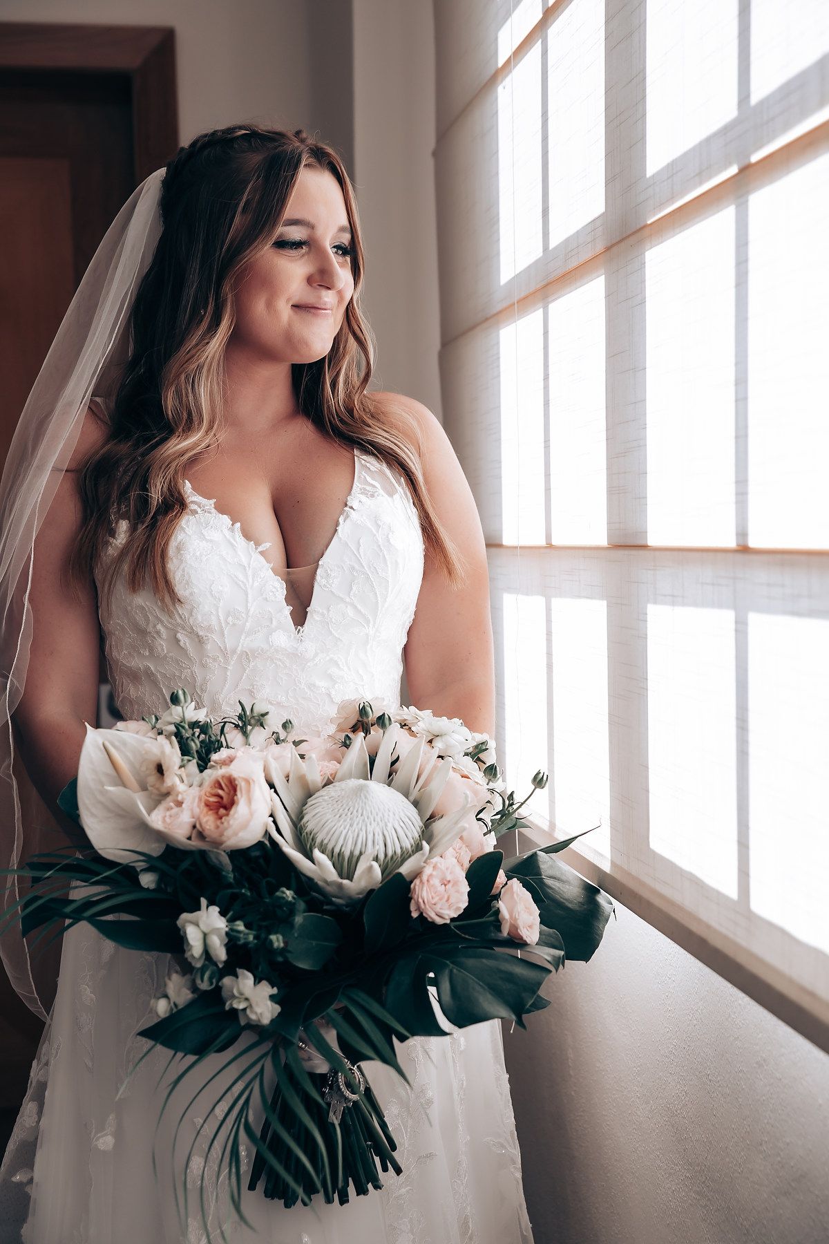 Elegant bridal portraits by a window showing details of a white lace wedding dress and floral bouquet.
