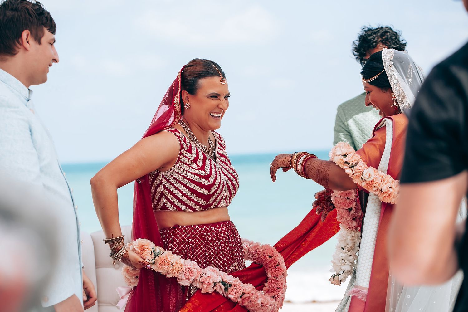 Beachside wedding ceremony moments with guests in vibrant red and traditional attire.