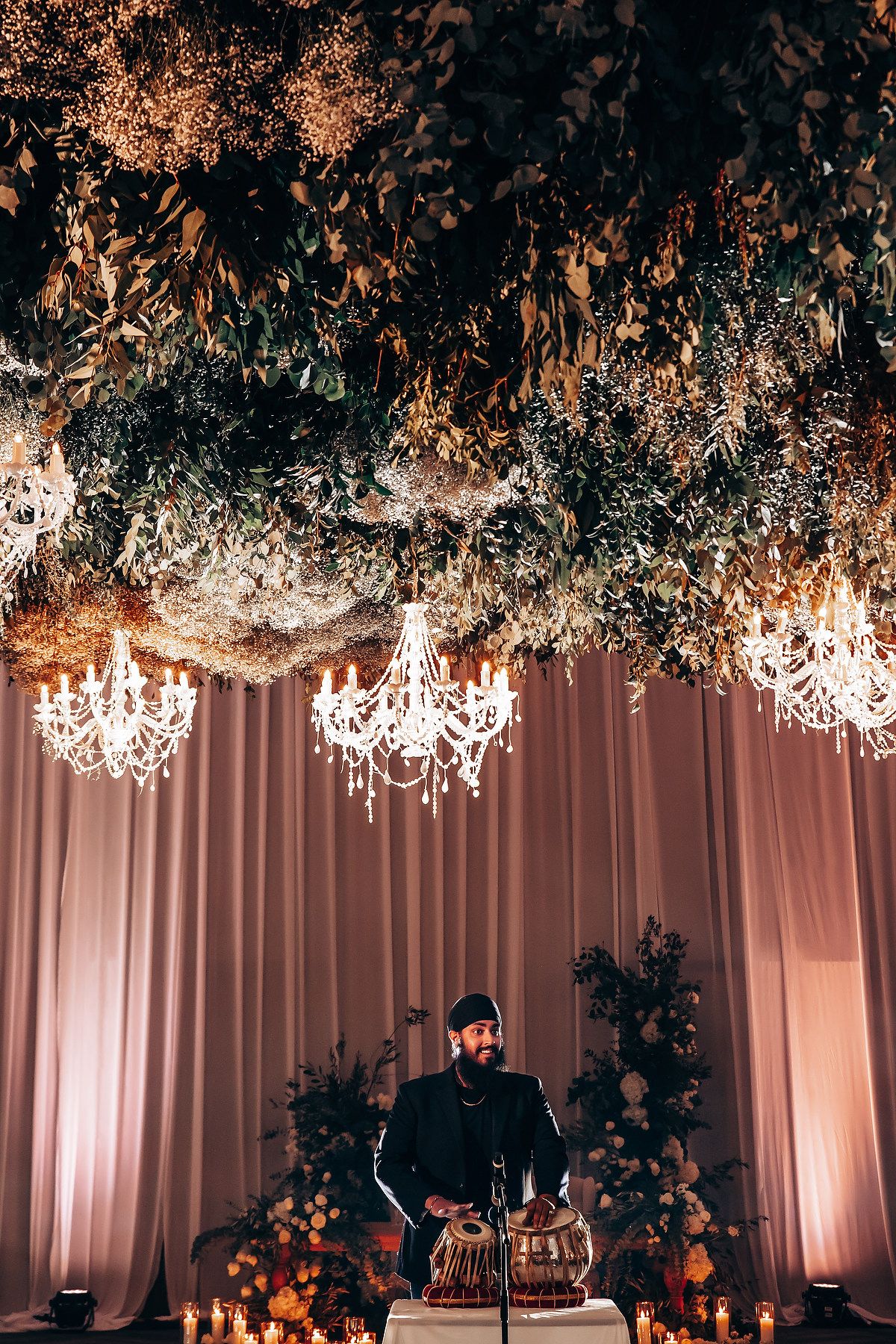 Elegant wedding reception decor with crystal chandeliers and floral arrangements hanging from white draped ceiling.