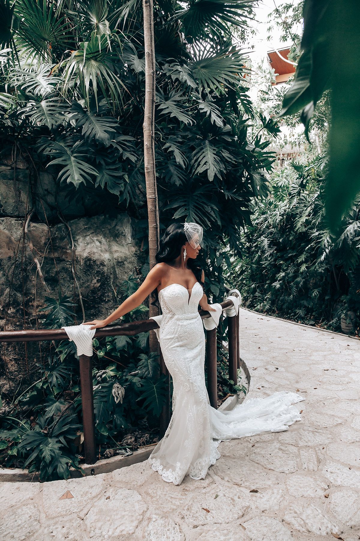 A white wedding dress flows gracefully against a lush tropical garden backdrop.