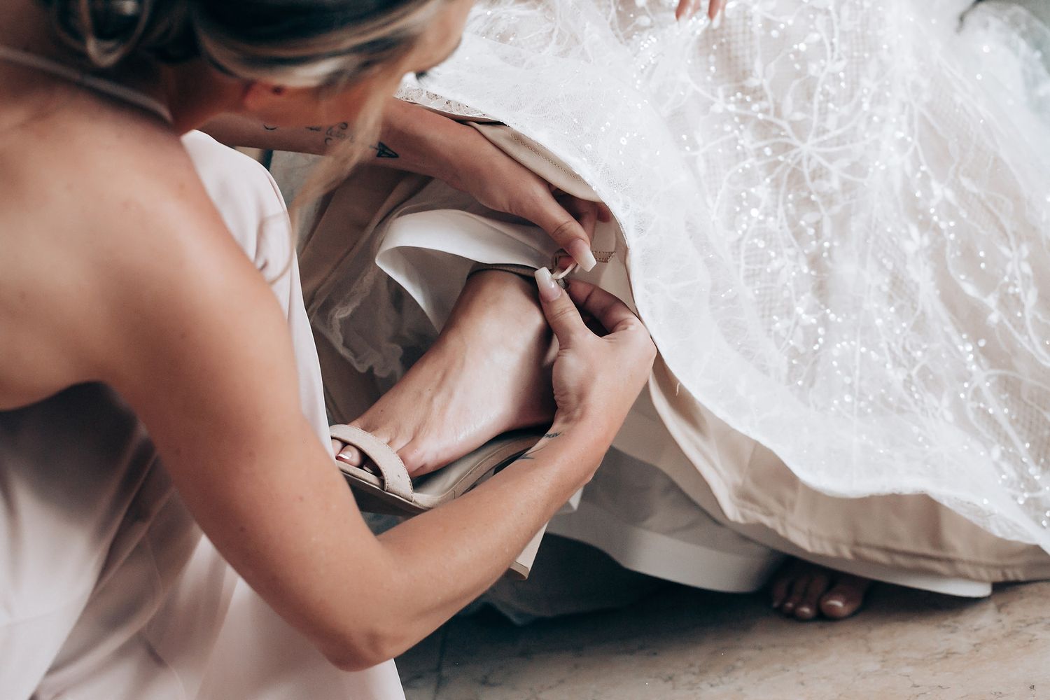 Close-up view of hands delicately adjusting a white wedding dress with intricate lace details.