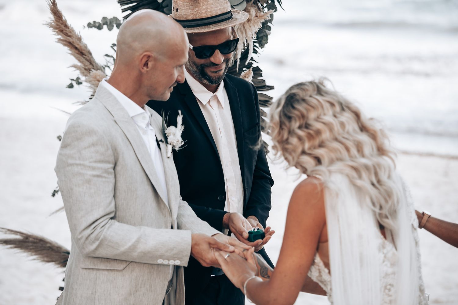 An intimate beach wedding ceremony under palm trees with guests watching the exchange of vows.